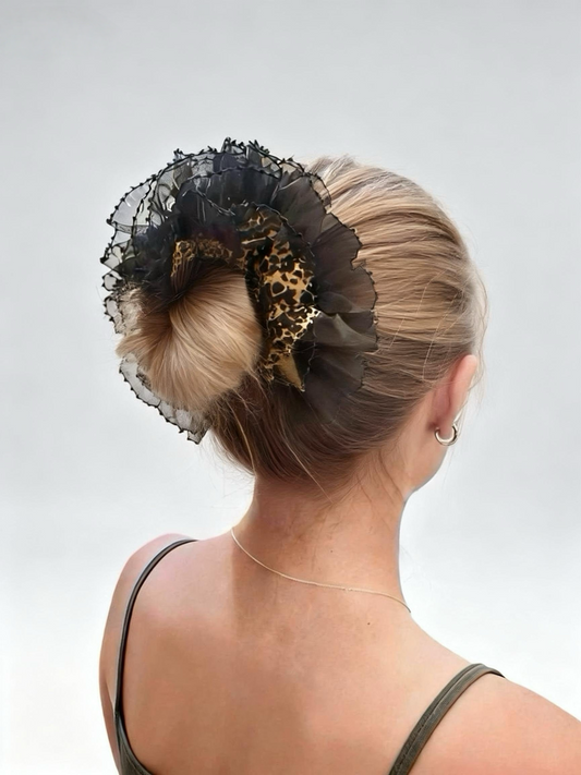 Person with a stylish hair bun featuring black lace and leopard print scrunchie against a plain background