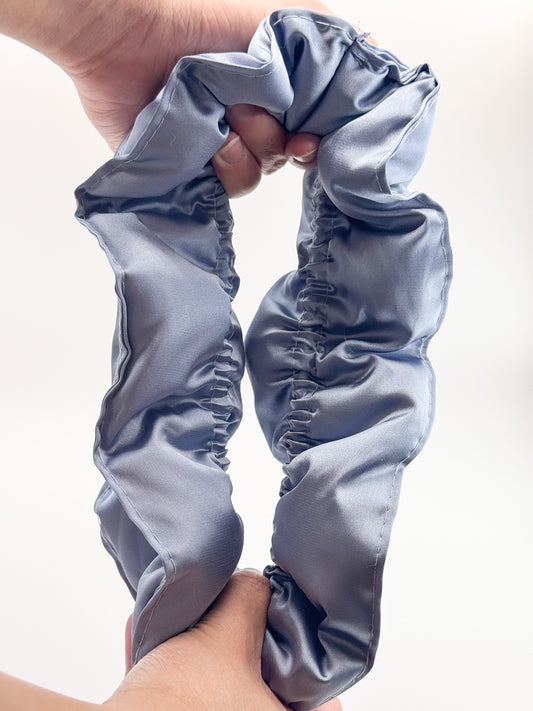 A blue satin pillow scrunchie held by a hand against a white background