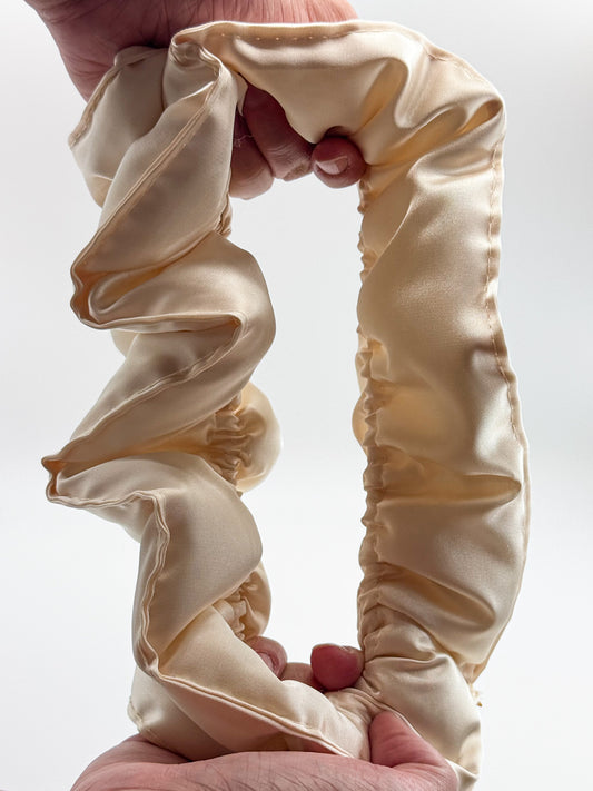 Beige satin pillow scrunchie held by hands against a white background
