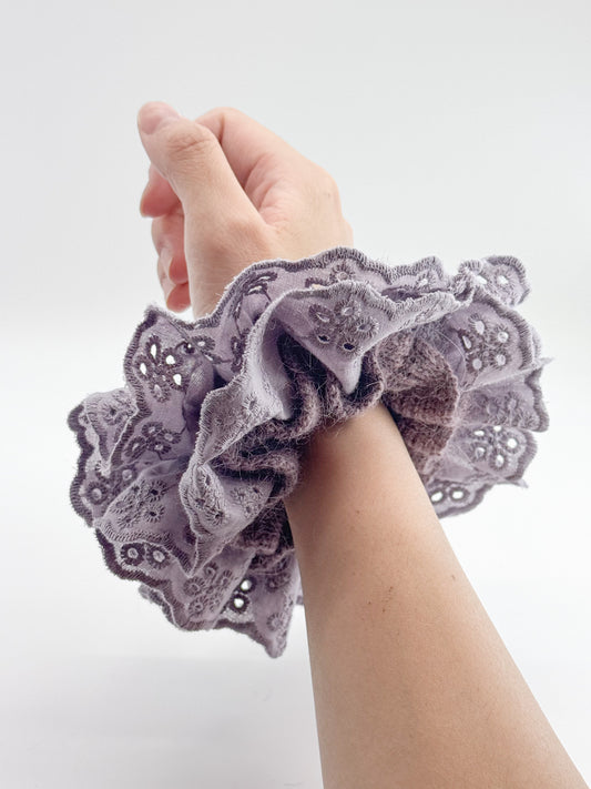 Hand wearing a purple lace scrunchie on a white background