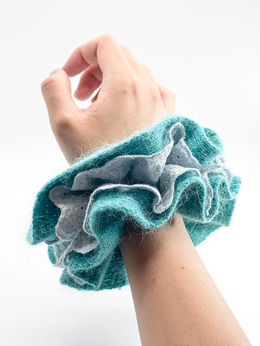 Hand wearing a blue knit lace scrunchie on a white background