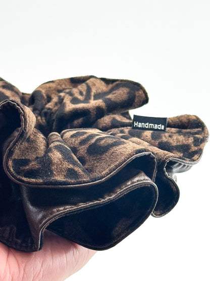 Brown leopard leather scrunchie held by a hand with 'Handmade' label on a white background