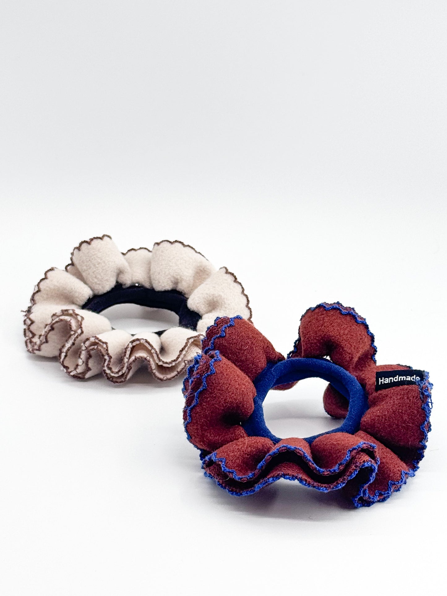 Two fabric scrunchies, one white and one red with blue accents, on a white background.