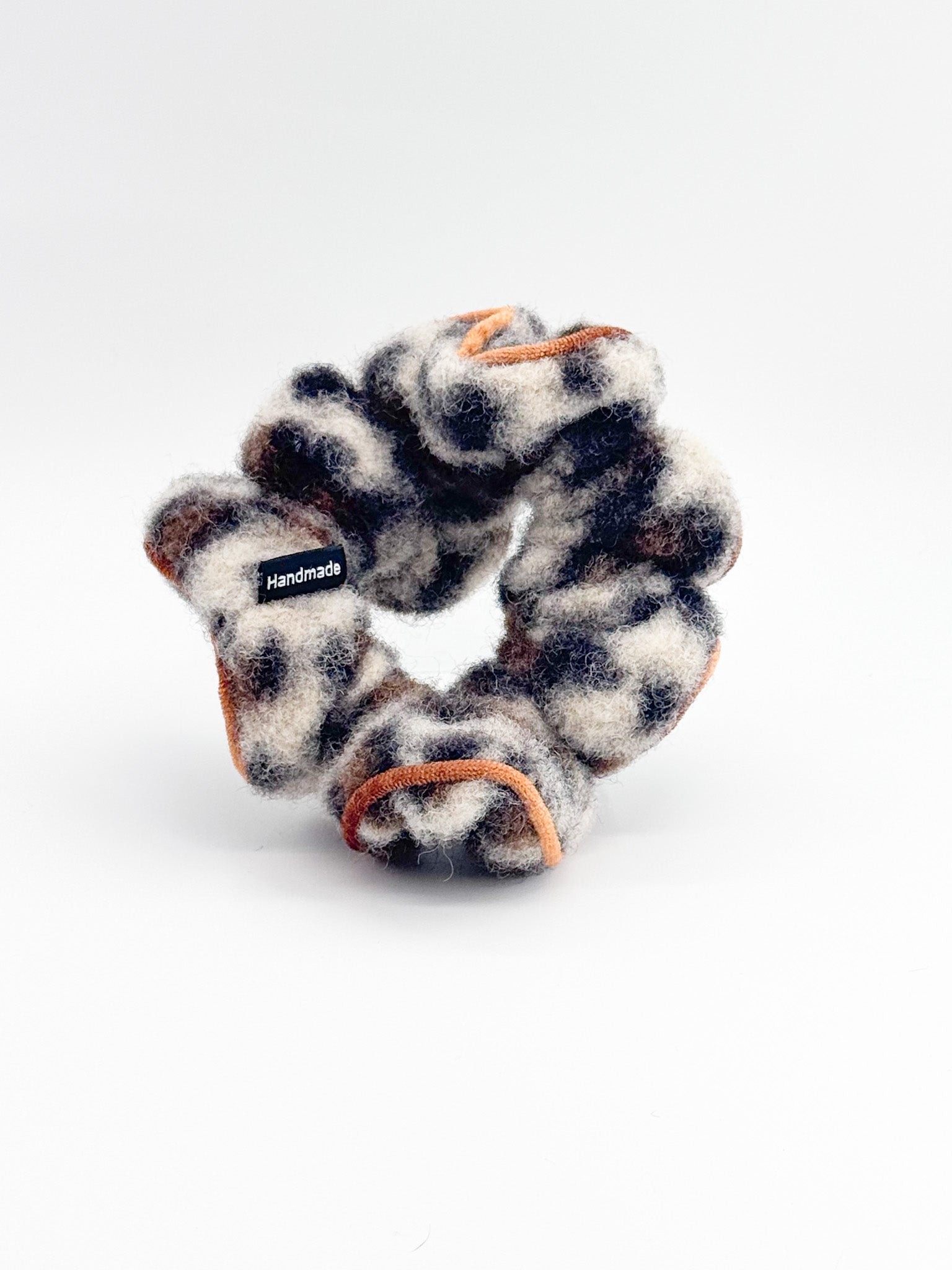 A leopard print with a orange-edge trim scrunchie on a white background