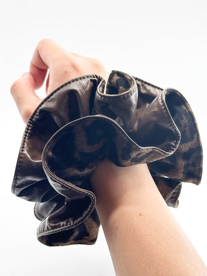 A leopard print leather large scrunchie on a wrist against a white background