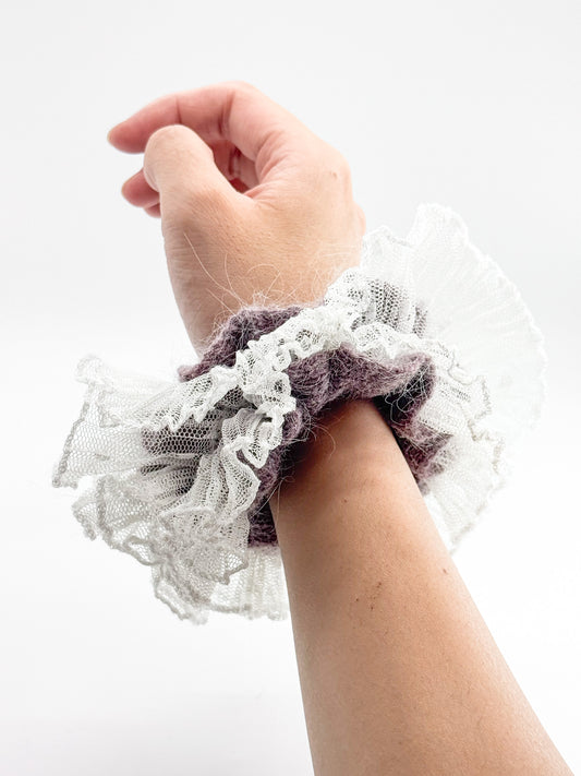 Hand wearing a purple knit lace scrunchie on a white background