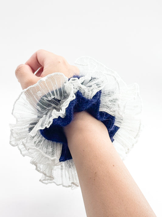 Hand wearing a blue and white lace scrunchie on a white background