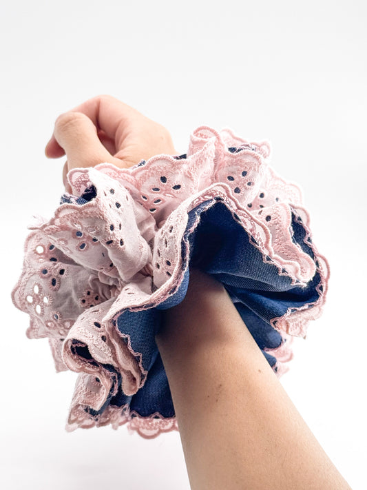 Hand holding a blue scrunchie with pink lace details against a white background