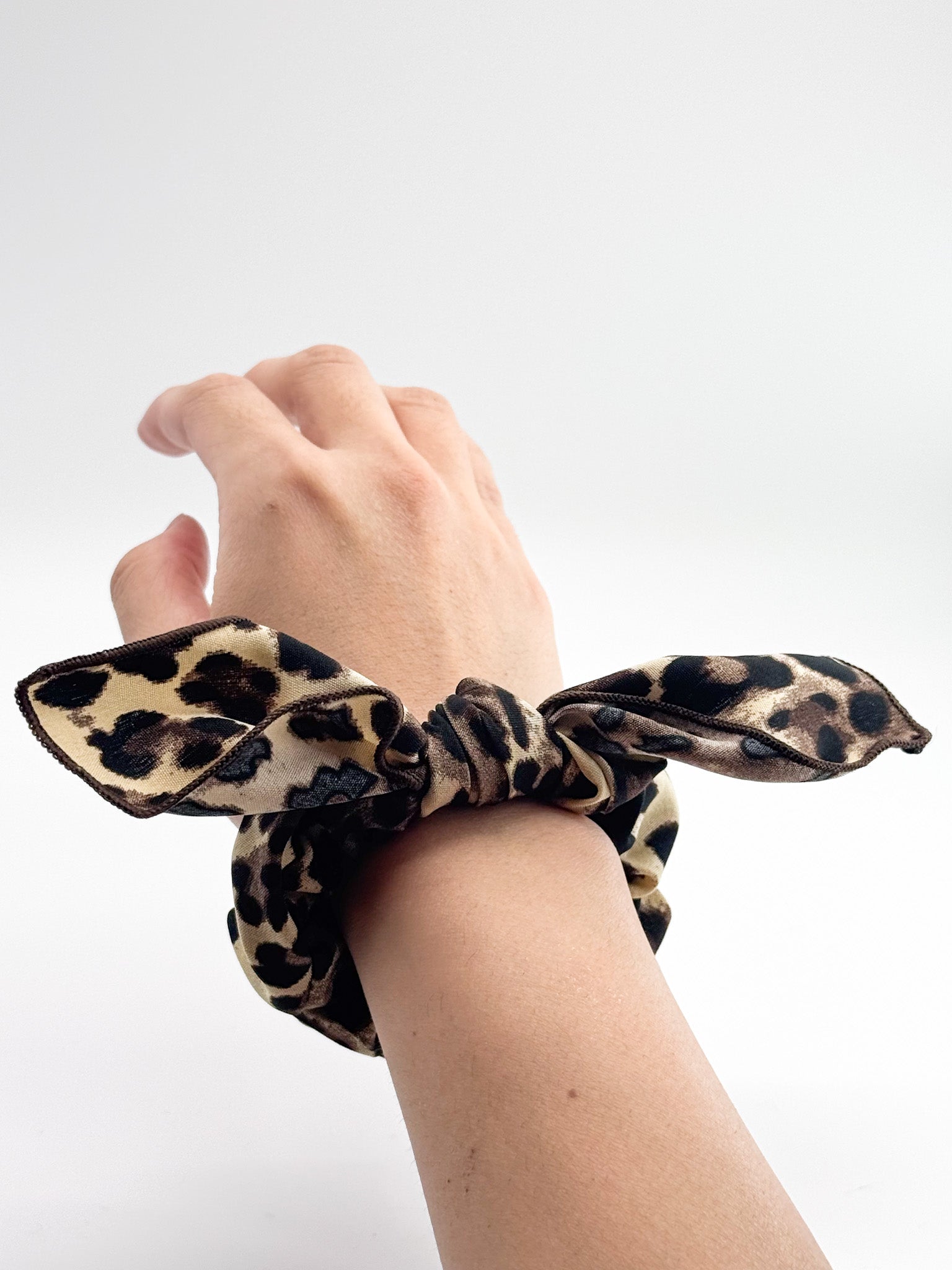 Leopard print scrunchie on a wrist against a white background