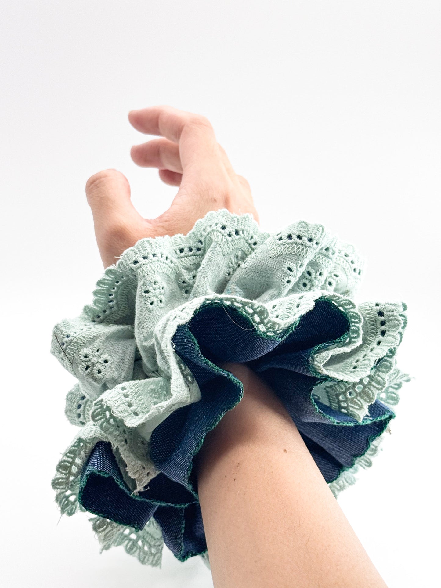 Hand wearing a blue and green lace scrunchie on a white background
