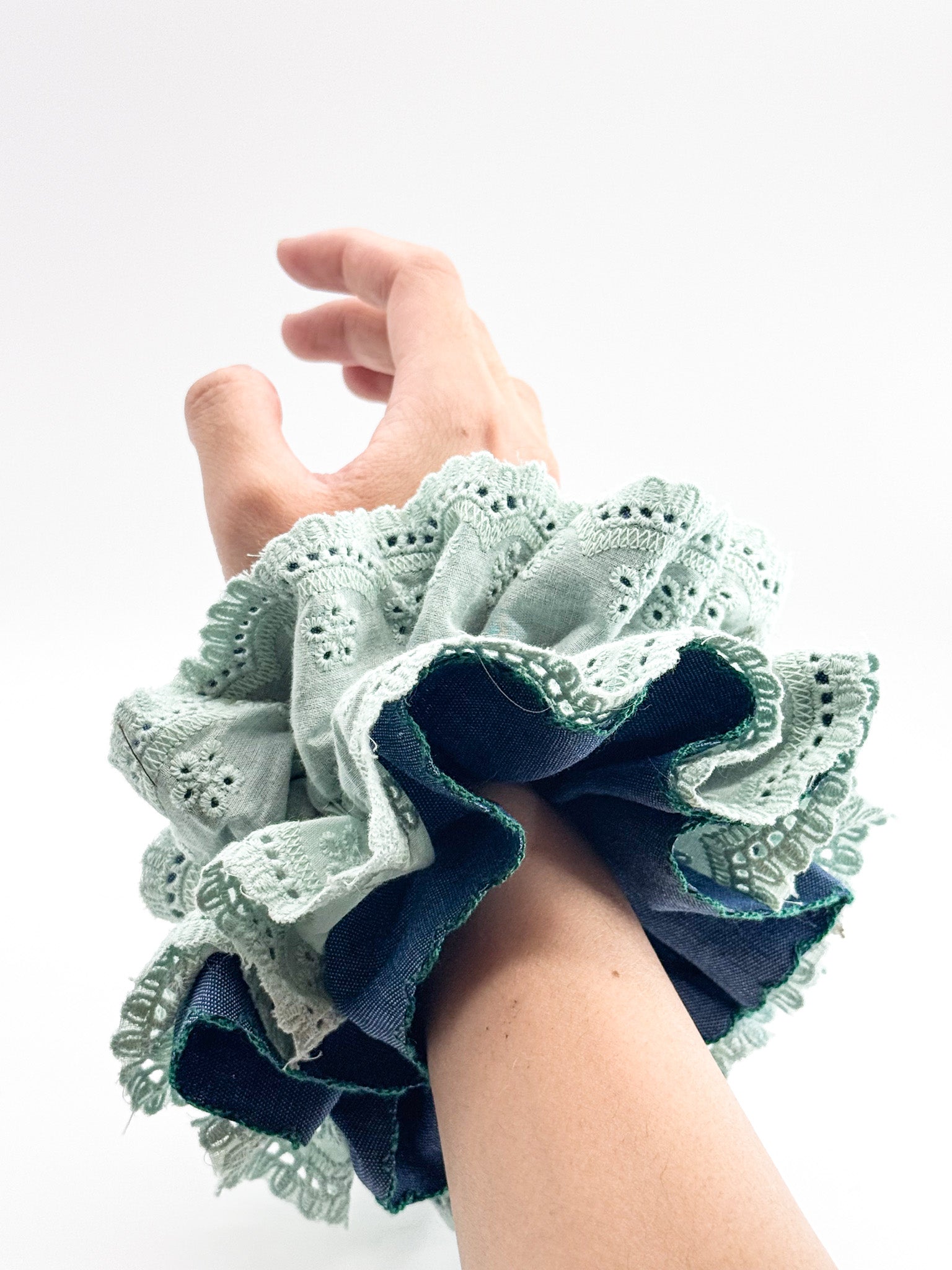 Hand wearing a blue and green lace scrunchie on a white background