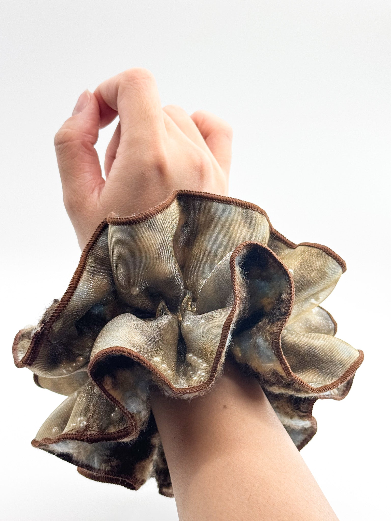Hand wearing a textured, ruffled srunchie against a plain background