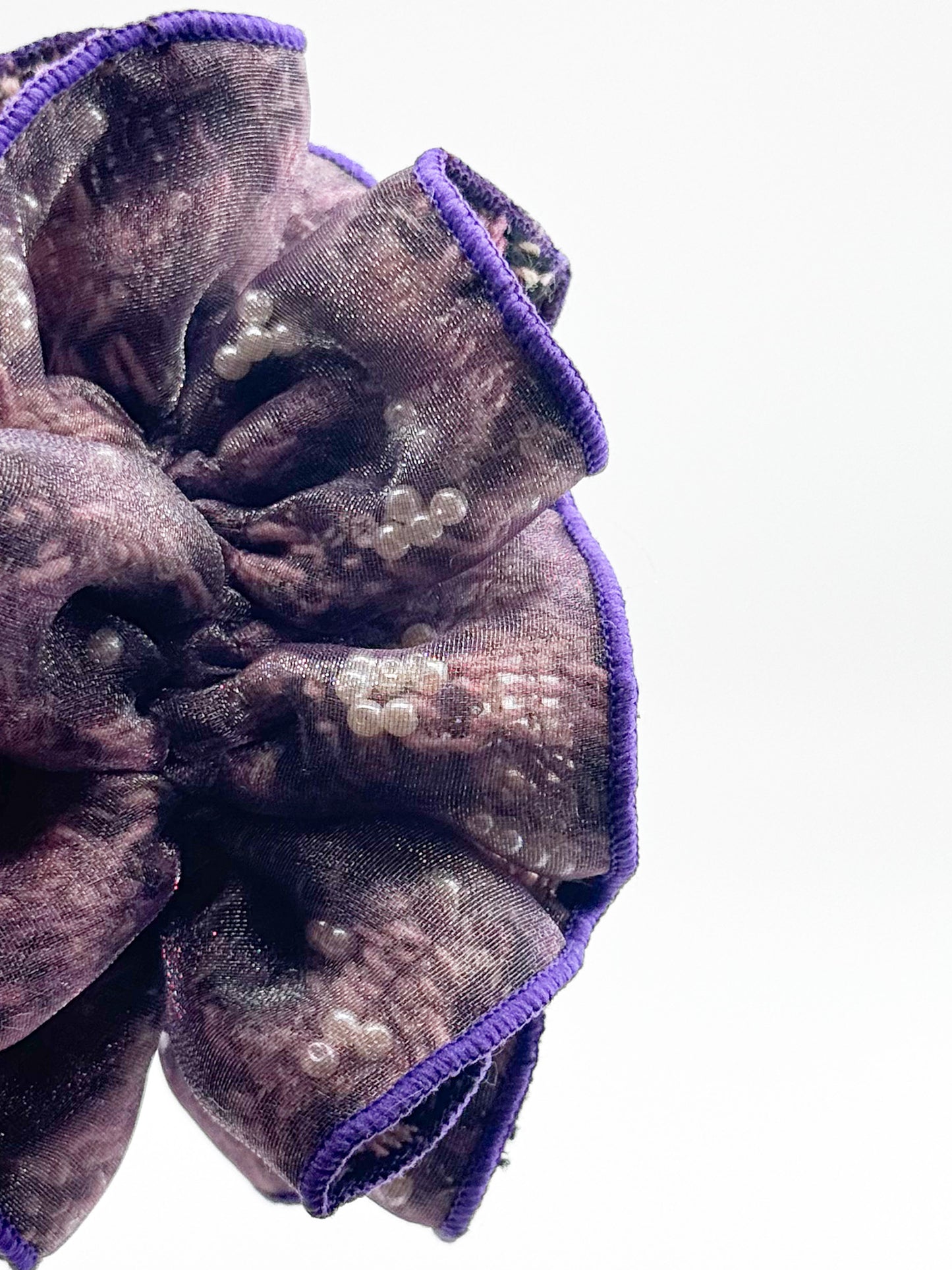 Scrunchie with purple trim and pearl-like embellishments on a white background