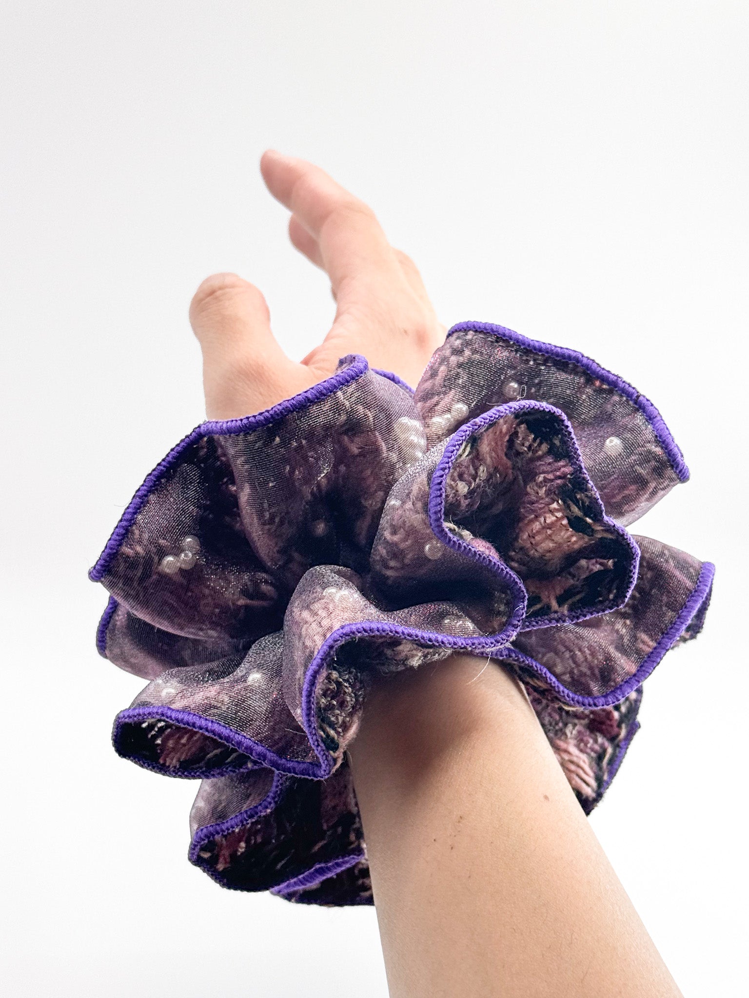 Hand wearing a purple-rimmed scrunchie on a white background