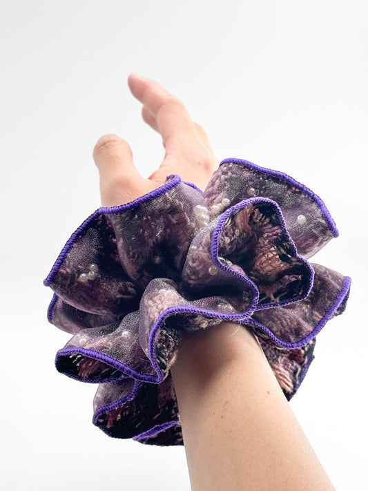Hand wearing a purple-rimmed scrunchie on a white background