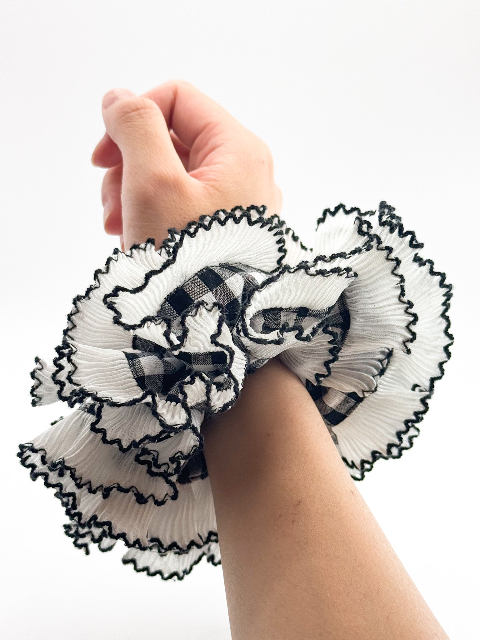 Hand wearing a decorative white and black large scrunchie with plaid patterns on a white background